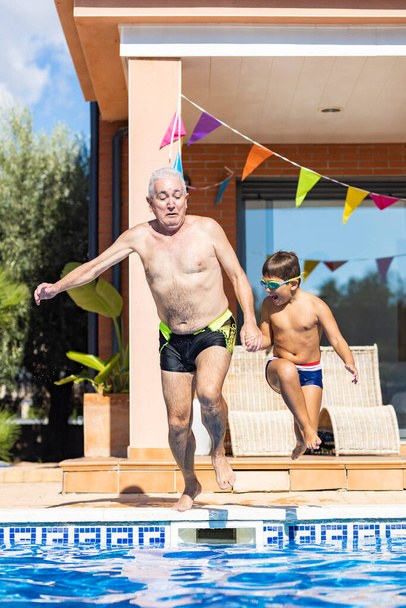 Grnadfather ja pojanpoika hyppäävät uima-altaaseen kesäpäivänä - Valokuva, kuva