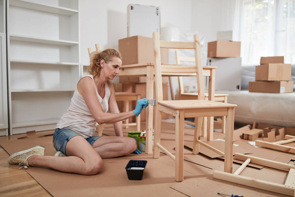 Frau streicht und montiert Möbel in neuer Wohnung, zieht ein und ist fleißig. - Foto, Bild