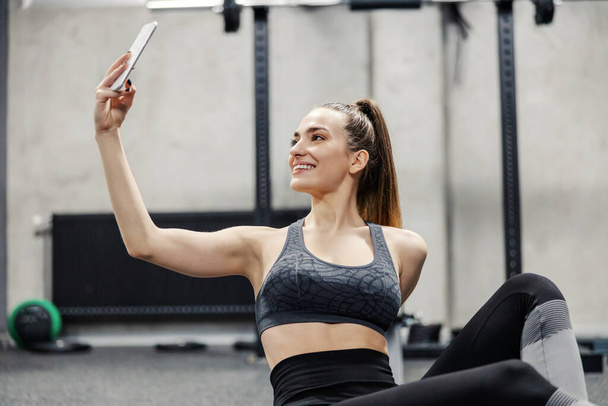 Fitness and social networks. Close up photo of beautiful female in sportswear takes photos of herself during training. She posts photos and videos from the training on social networks. Sports bra - Photo, Image