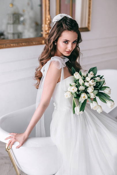 Young bride in wedding dress holding bouquet of white tulips in studio - Foto, imagen
