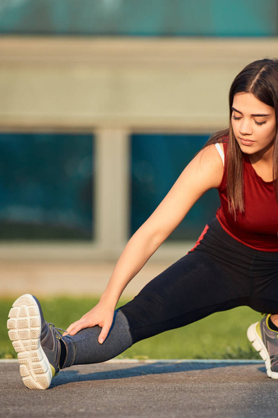 Young sporty woman stretching and exercising in urban park. - Photo, Image