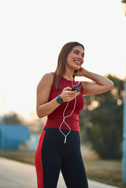 Modern young woman with cellphone making pause during jogging exercise. - 写真・画像