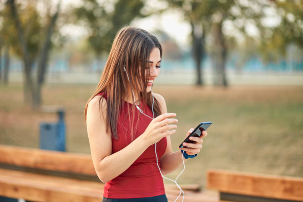 Modern young woman with cellphone making pause during jogging exercise. - Zdjęcie, obraz