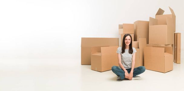 happy young woman sitting on floor surrounded by moving boxes - Photo, image