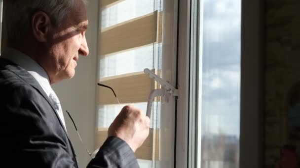 Un homme âgé aux cheveux gris se tient près de la fenêtre dans le bureau - Séquence, vidéo