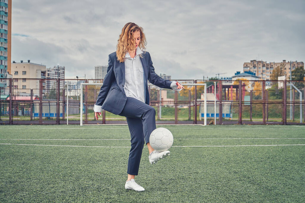 girl in an office suit hitting hitting soccer ball on the stadium field. concept - Foto, afbeelding