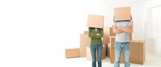 pareja con cajas en la cabeza de pie en su nueva casa, brazos cruzados contra el pecho - Foto, imagen