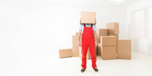 Frontansicht eines Lieferanten, der in einem neuen Haus steht und seinen Kopf mit einer Schachtel bedeckt. Kopierraum vorhanden - Foto, Bild