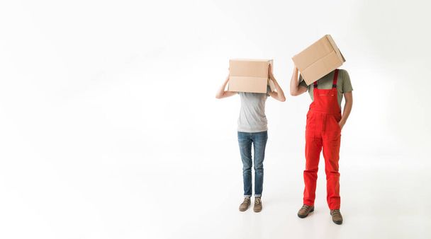 woman and man standing and holding cardboard boxes on top of their heads, on white background. copy space available - Zdjęcie, obraz