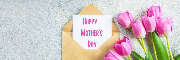 Conceito do feriado do dia das mães. Flores de tulipas rosa e cartão vazio no fundo de concreto. Cartão de felicitações para o Dia das Mulheres ou das Mães. Deitado plano, vista superior - Foto, Imagem