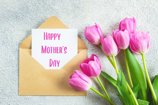Mother's day Holiday Concept. Pink tulips flowers and empty card on concrete background. Greeting card for Womens or Mothers Day. Flat lay, top view - Photo, Image
