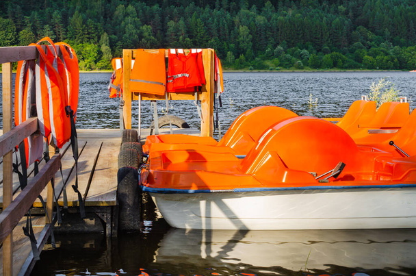 Catamaranes naranjas en el lago amarrados en el muelle. Barcos de recreo con chalecos salvavidas. - Foto, imagen