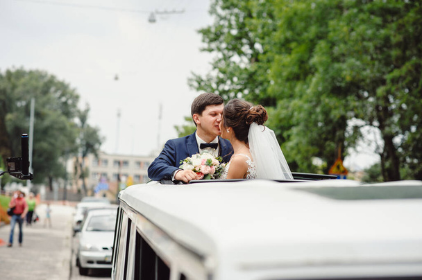 Nádherný elegantní svatební pár líbání a objímání na střeše bílé limuzíny na městské silnici. Právě ženatý. - Fotografie, Obrázek