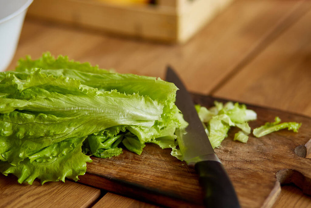Tabla de madera y cuchillo con hoja de corte de lechuga de ensalada, Preparación de ensalada de verduras en la cocina en casa, concepto de comida saludable, vegana o dieta. Vista superior. - Foto, imagen