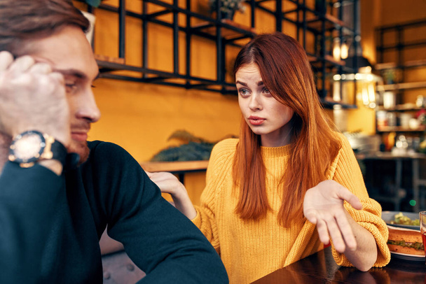 щаслива жінка в светрі жестикулює руками веселі емоції і чоловік в светрі сидить в кафе
 - Фото, зображення