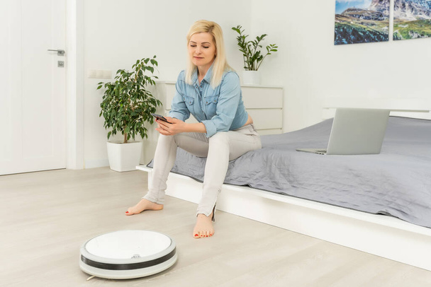 Robotic vacuum cleaner cleaning the room while woman resting - 写真・画像