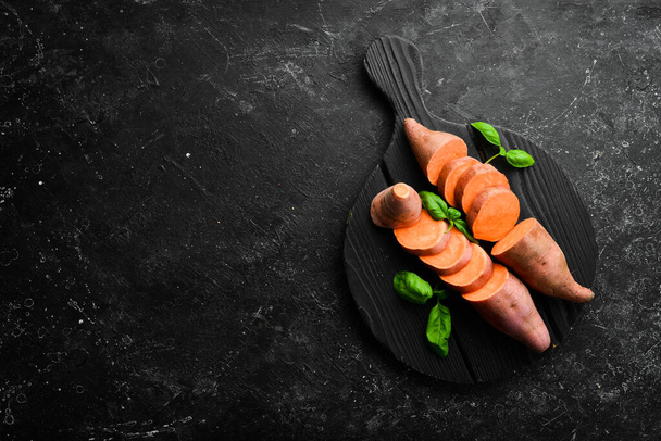 Raw sweet potatoes and basil on a black stone background. Top view. Free space for your text. - Foto, Bild