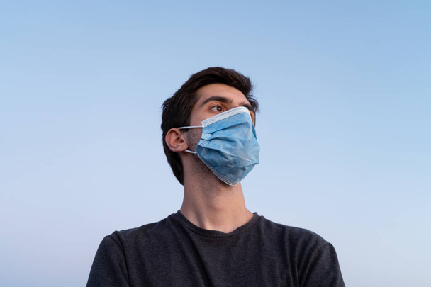 Low angle shot of a young man wearing a mask with light blue sky in the background. - Photo, Image