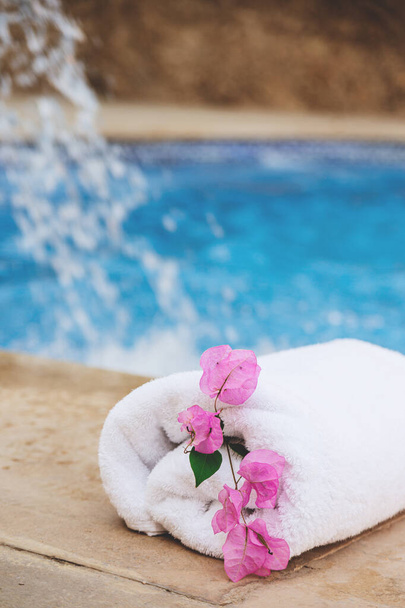 Valkoinen pyyhe vaaleanpunaisia kukkia lähellä kylpylä allas hotellissa lomalla - Valokuva, kuva