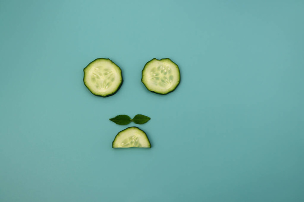 Circles and semicircles of a cucumber with green mint leaves on a light blue background. Funny background. - Photo, Image