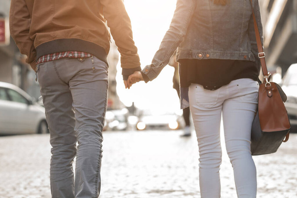 Couple holding hands and walking on a sidewalk. - Фото, изображение