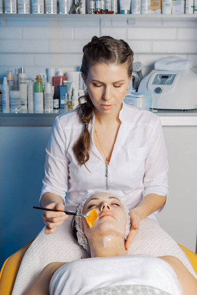Профессиональная косметолог наносит маску с кистью на лицо клиентов. - Фото, изображение