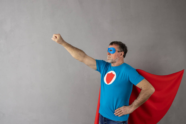Senior man wearing superhero costume against grey concrete wall background. Success and winner concept - Фото, зображення