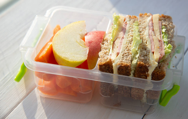 Lunch box with vegetables, fruits and sandwiches on wooden table - Photo, Image