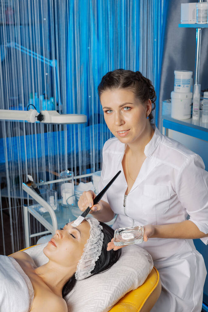 Mujer esteticista profesional aplica máscara con cepillo a la cara de los clientes. - Foto, imagen