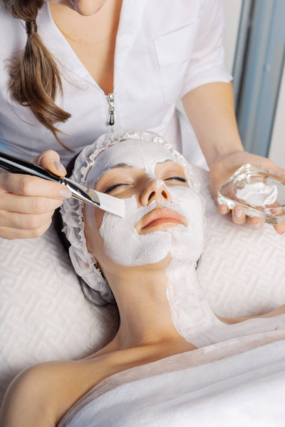 プロの美容師の女性は、クライアントの顔にブラシでマスクを適用します. - 写真・画像