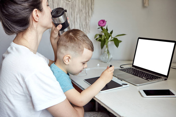 Kobieta z dzieckiem pracuje przy komputerze. Pojęcie pracy w domu i wychowaniu rodzinnym. Mama i syn pracują na tablecie graficznym i laptopie w domu.. - Zdjęcie, obraz