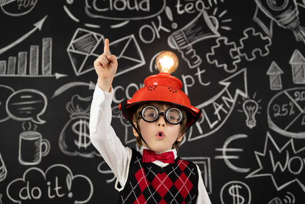 Smart child pretend to be businessmen. Funny kid wearing helmet with lightbulb. Education, artificial intelligence and business idea concept - 写真・画像