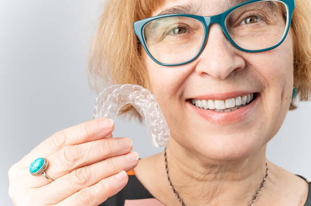 Счастливая пожилая женщина надевает прозрачные съемные брекеты. Косметическая стоматология для всех возрастов - Фото, изображение
