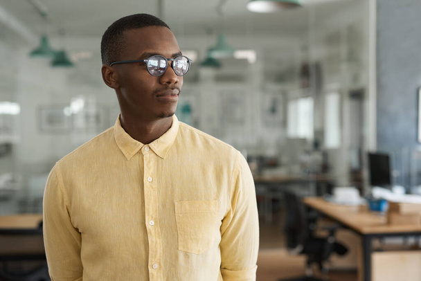 Focused young African businessman thinking about work while working in a large modern office after hours - 写真・画像