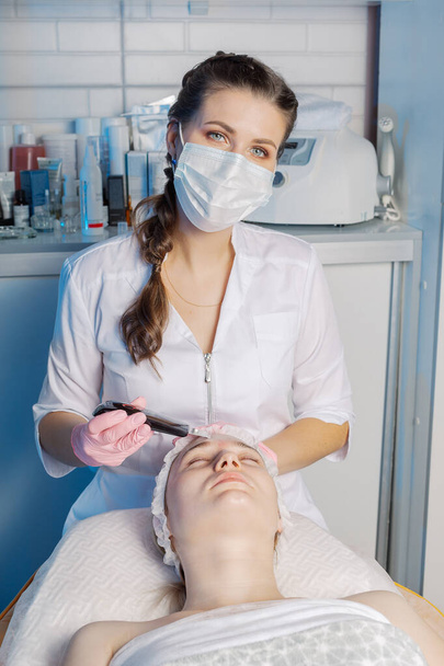 Профессиональный косметолог проводит ультразвуковую процедуру очистки лица для женщины. - Фото, изображение