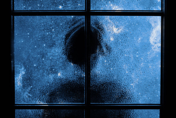 Silhueta escura de criança sozinha, isolada atrás da porta de vidro. Imagem abstrata de tristeza, apatia, depressão, melancolia. Muitas estrelas e nebulosas no quarto escuro. Elementos desta imagem fornecidos pela NASA. - Foto, Imagem