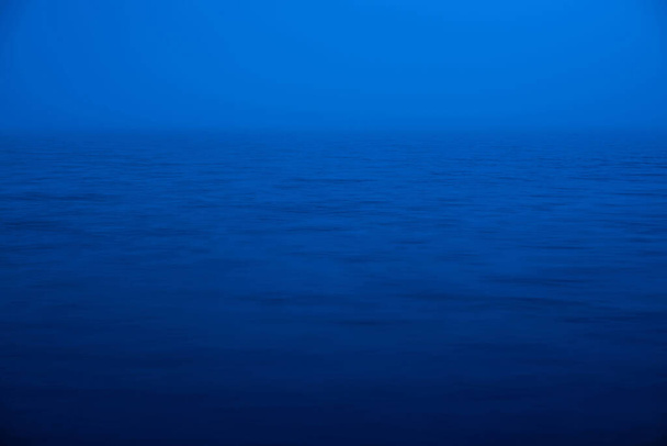 Ondulation de l'eau fond de la nature. Texture naturelle de la mer de couleur bleue classique. Eau calme bleu profond au crépuscule gros plan. Image méditative de brouillard dense au-dessus du lac. Paillettes de lumière douce sur la surface de l'eau. - Photo, image