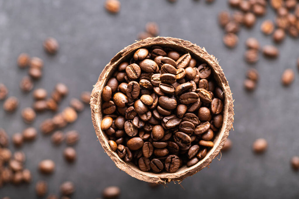 black coffee beans arabica, aromatic in a coconut dish, sprinkled beans on the table, close-up, top view - Foto, Imagen
