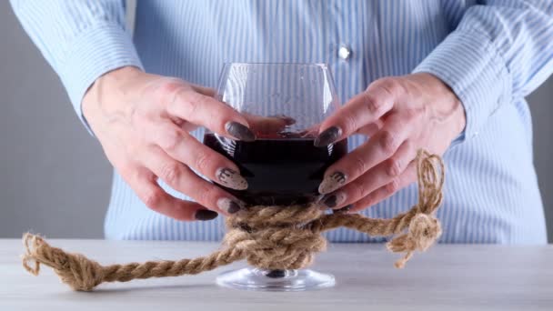 le mani femminili che tengono il bicchiere di vino sono legate con una corda di iuta. Il concetto di dipendenza da alcol. Il problema del trattamento dell'alcolismo - Filmati, video