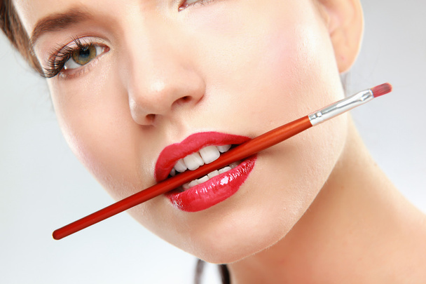 Woman's lips holding make up brush - Foto, afbeelding