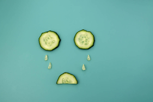 Circles and semicircles of a cucumber with green mint leaves on a light blue background. Sad cucumber. - Photo, Image