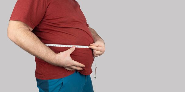 homem gordo mede o tamanho do abdômen com um centímetro de fita métrica. as pessoas sofrem de excesso de peso. banner, espaço de cópia - Foto, Imagem