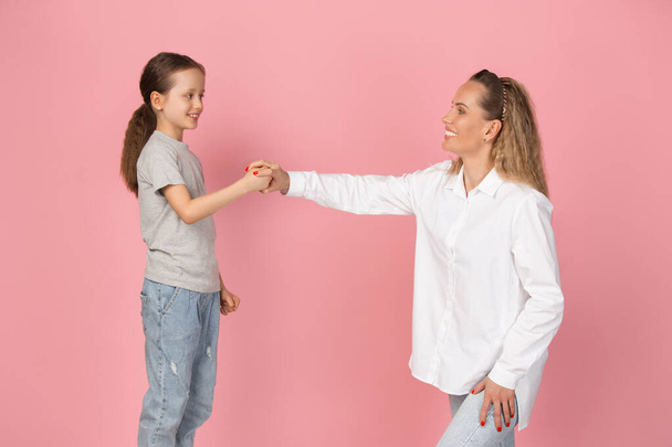 Young woman and girl, mother and daughter isolated over pink background. - Foto, Bild
