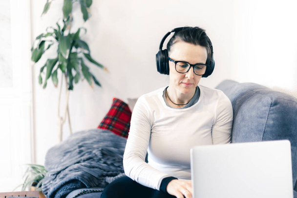 woman working on the sofa with laptop and headphones - Photo, Image