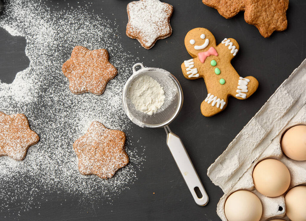 Star shaped baked gingerbread cookies sprinkled with powdered sugar on a black table, top view - Foto, Bild