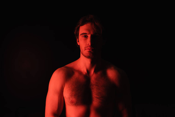 red lighting on sexy shirtless man looking at camera isolated on black  - Photo, Image