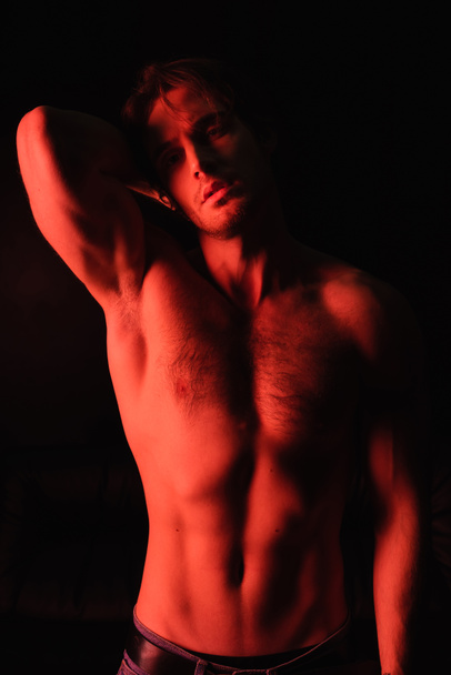 red lighting on sexy and muscular man standing isolated on black  - Φωτογραφία, εικόνα