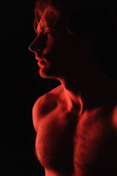 red lighting on sexy shirtless man looking away isolated on black  - Фото, зображення
