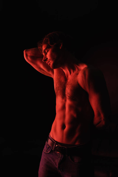 red lighting on body of muscular man standing isolated on black  - Foto, Bild