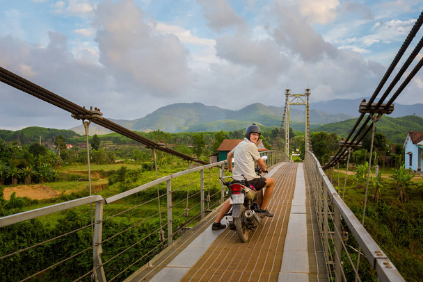 Schöne junge kaukasische Touristin mit einem Motorrad auf einer Flussbrücke im Nationalpark Phong Nha Ke Bang, Vietnam. Foto der ländlichen Landschaft in Südostasien - einer der schönsten vietnamesischen Orte. - Foto, Bild